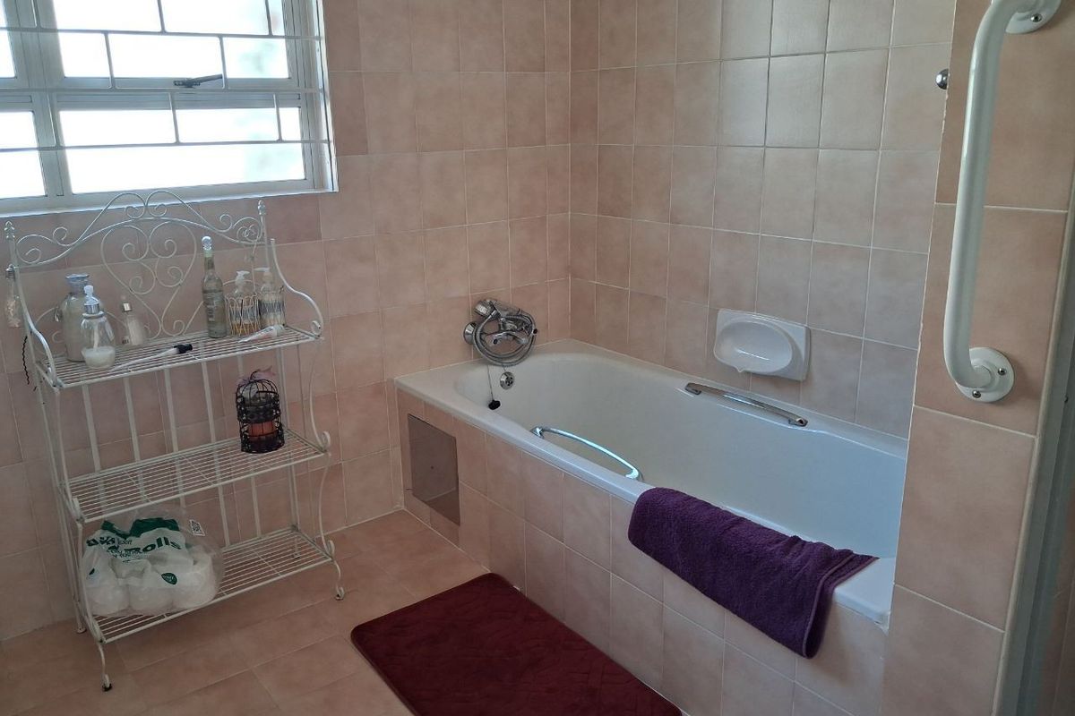 A functional bathroom featuring a built-in bathtub with a wall-mounted grab rail, tiled walls, and a window with security bars.