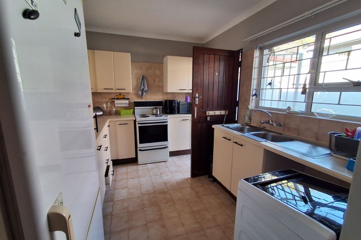 Functional kitchen featuring cream cabinetry, tiled splashbacks, a double-basin sink, and a freestanding stove, with direct access to the exterior.