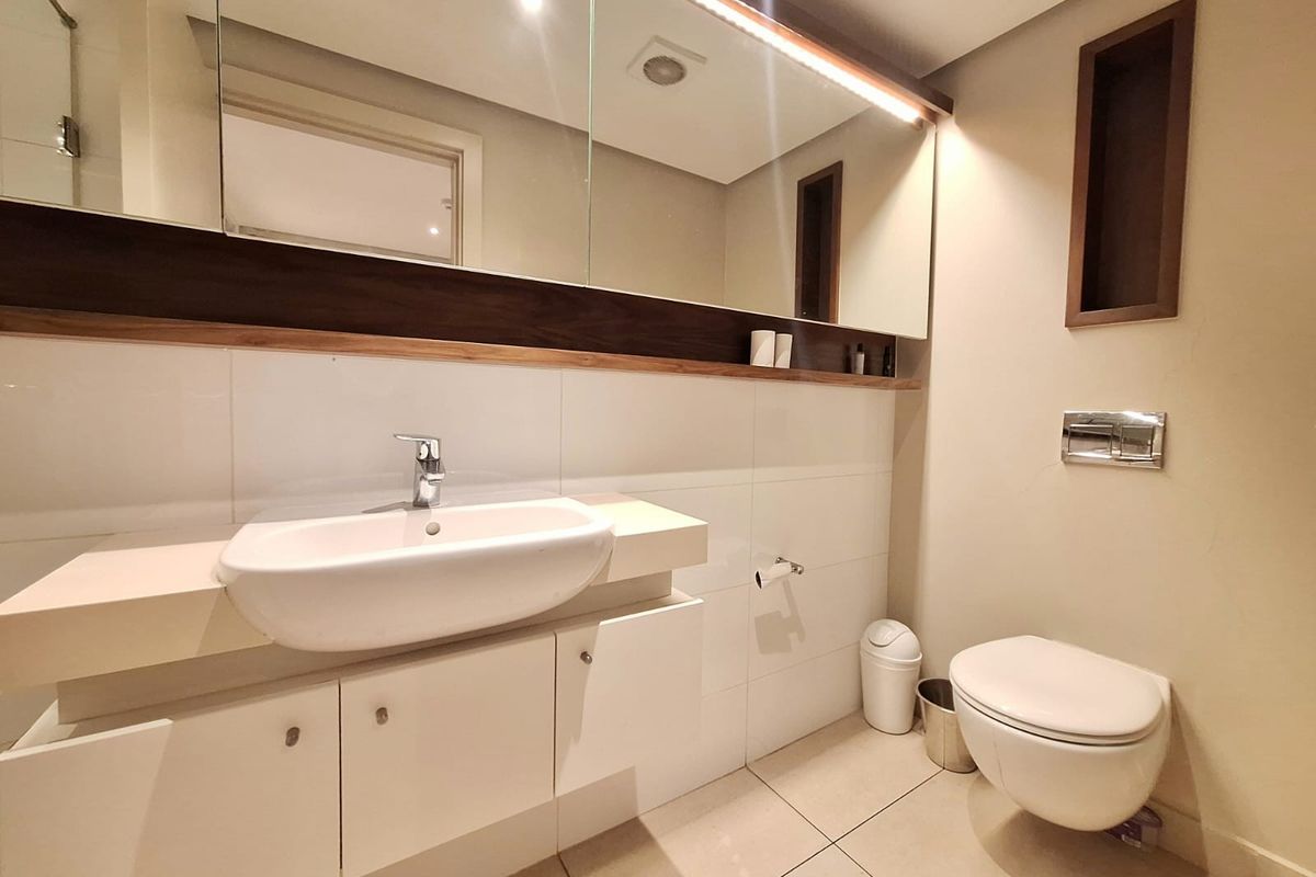 Modern bathroom featuring a wall-mounted vanity with integrated basin, large mirror with built-in lighting, and a wall-hung toilet.