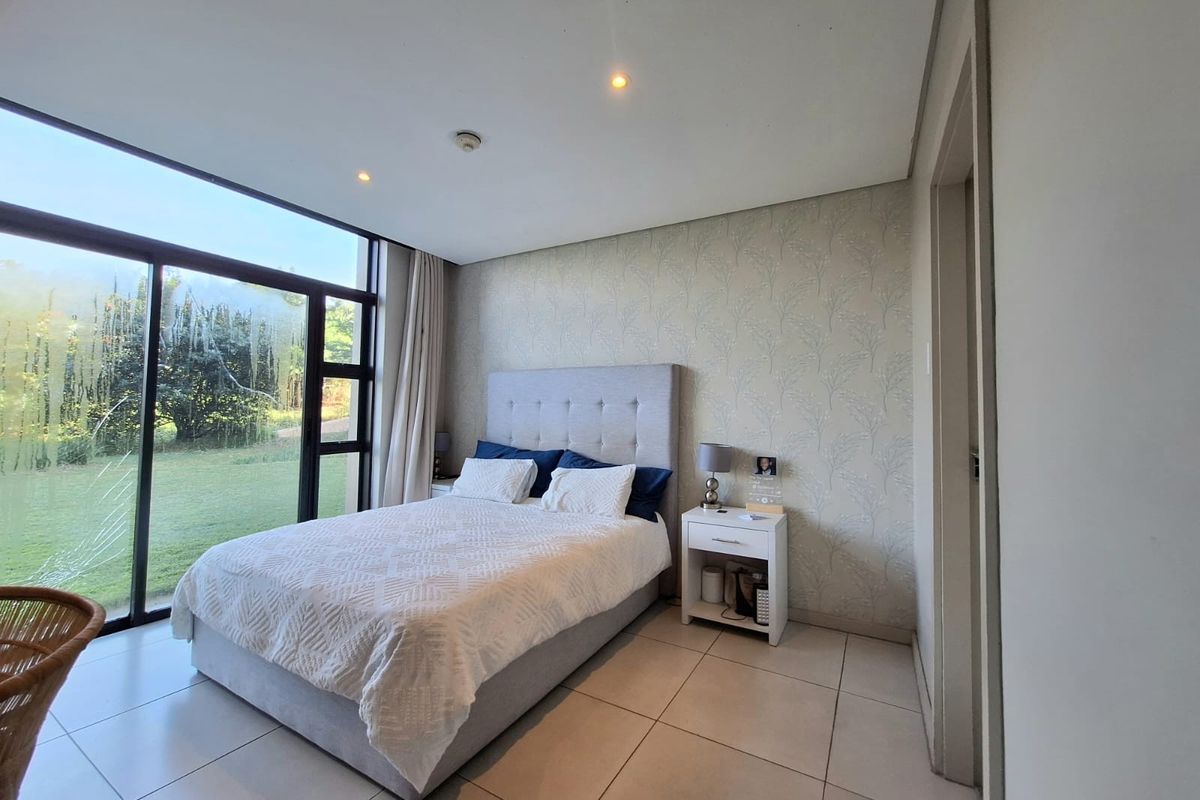 A bright bedroom featuring large floor-to-ceiling sliding glass doors with garden views, tiled flooring, and a feature wallpaper wall.