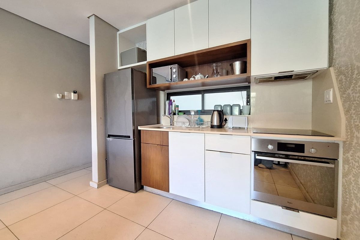Modern kitchen featuring white and wood-tone cabinetry, integrated oven, electric hob, extractor fan, and tiled flooring in an open-plan layout.
