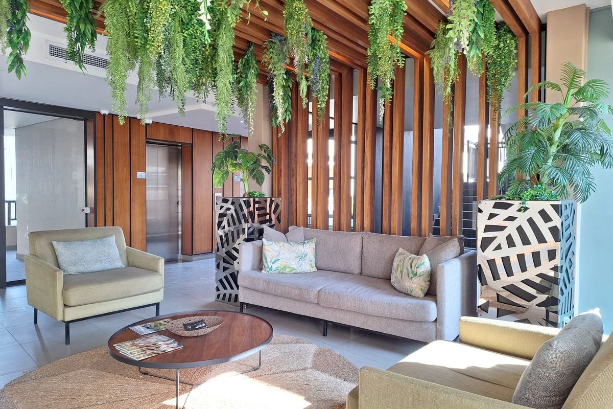 Modern apartment lobby or communal lounge area featuring decorative timber slat wall paneling, integrated ceiling beams, and a stainless steel elevator entrance.