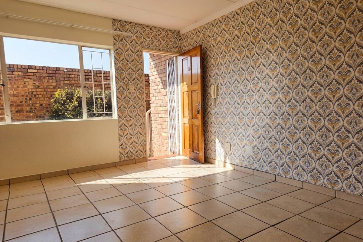 An empty living area featuring dated patterned wallpaper, tiled flooring, and direct access to an exterior entrance.