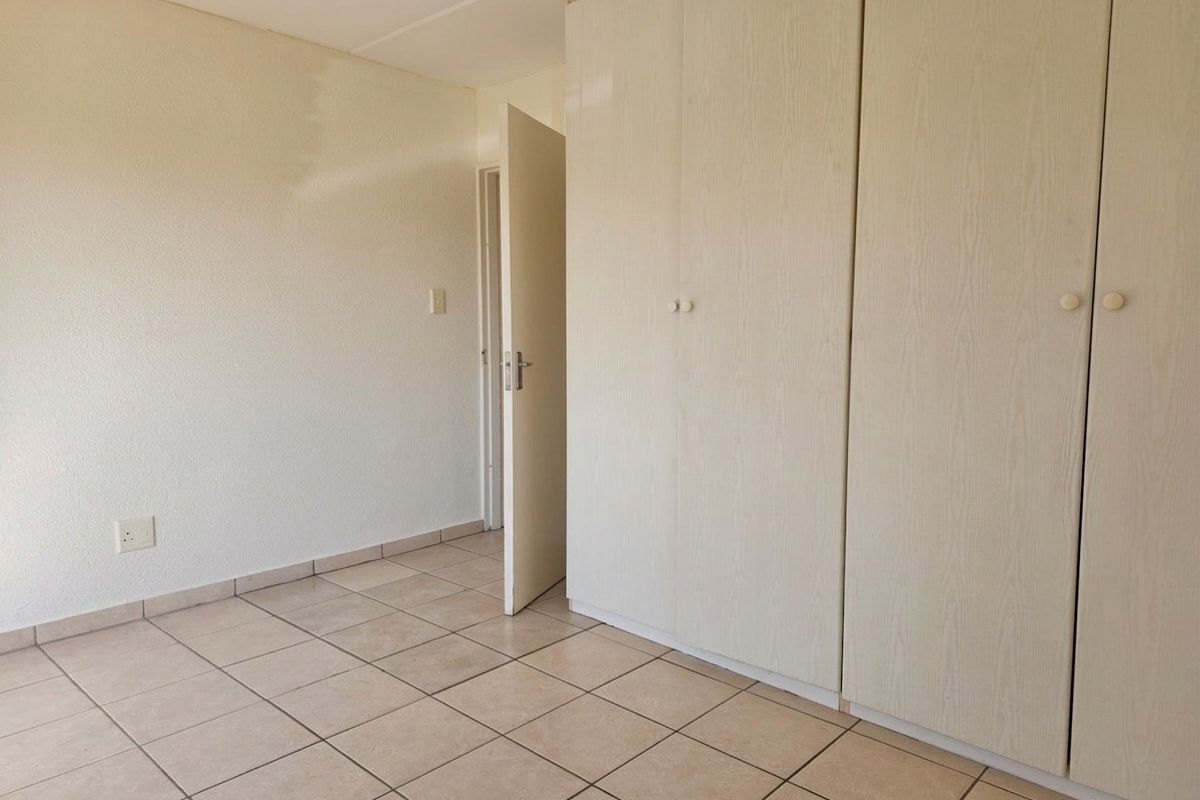 A bedroom featuring neutral floor tiles and built-in wooden cupboards, offering a clean and functional space.