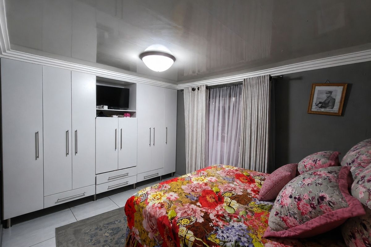 A well-maintained bedroom featuring extensive built-in white cabinetry, glossy ceiling finish, and large windows with curtain treatments.