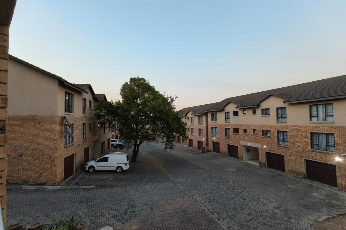 View of the apartment complex exterior featuring brick facades, tiled roofing, and a paved communal driveway with integrated garage access.