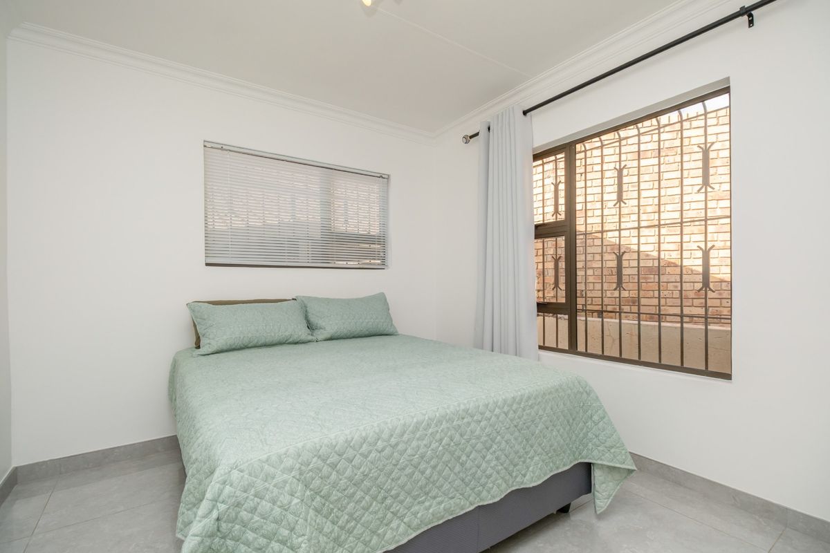 A bright bedroom featuring tiled flooring, a window with security bars, and neutral white walls.