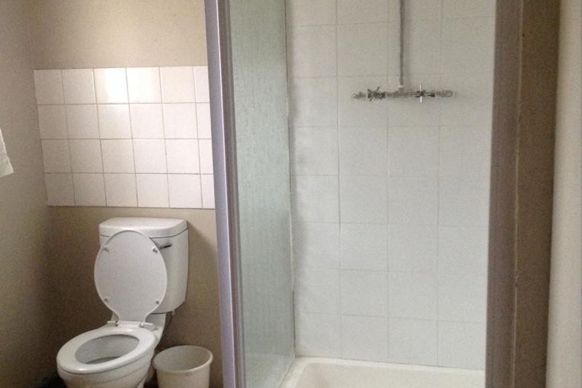 A functional bathroom featuring a shower enclosure with a tiled base and a standard toilet, requiring cosmetic updates to finishes and fixtures.