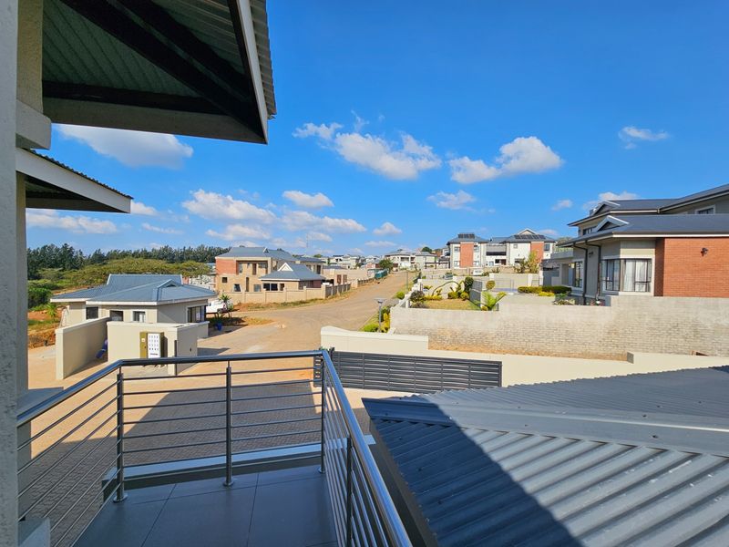 A modern elevated balcony featuring a stainless steel balustrade and tiled flooring, offering an expansive view over the surrounding residential estate.