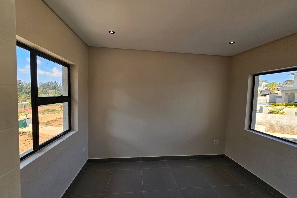 A bright, empty bedroom featuring neutral tiled flooring, recessed downlights, and large aluminium-framed windows offering natural light and exterior views.