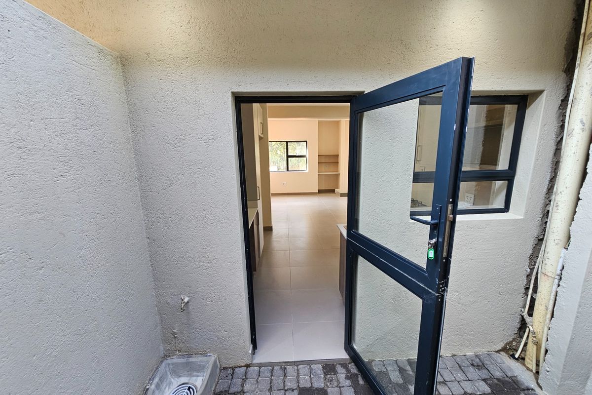A rear courtyard area featuring a paved surface, an external utility sink, and a modern aluminium door providing access to the interior living space.