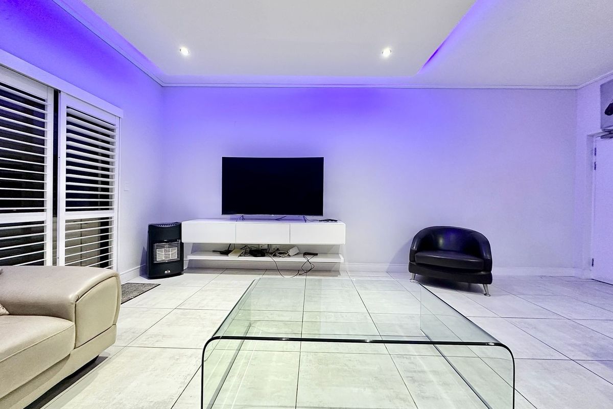 Modern living room featuring large format floor tiles, recessed ceiling with integrated LED accent lighting, and white plantation shutters.