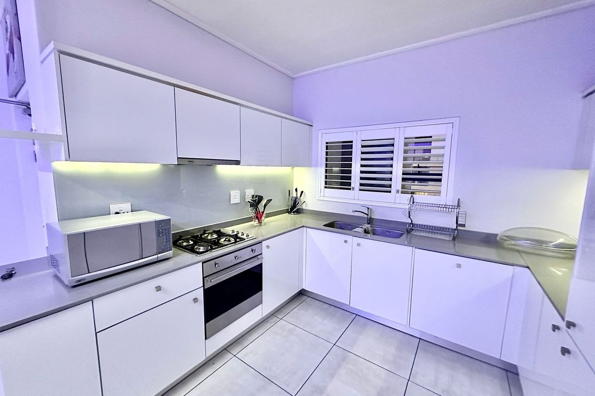 Modern kitchen featuring white cabinetry, stone countertops, gas hob, built-in oven, and integrated lighting with tiled flooring and shutter blinds.