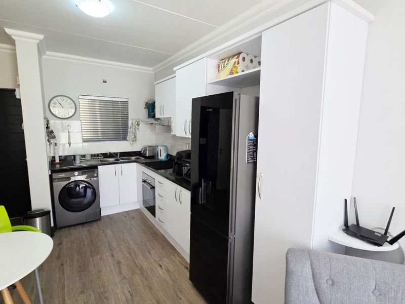 Compact kitchen featuring white cabinetry, dark countertops, integrated oven, extractor fan, and wood-look laminate flooring.