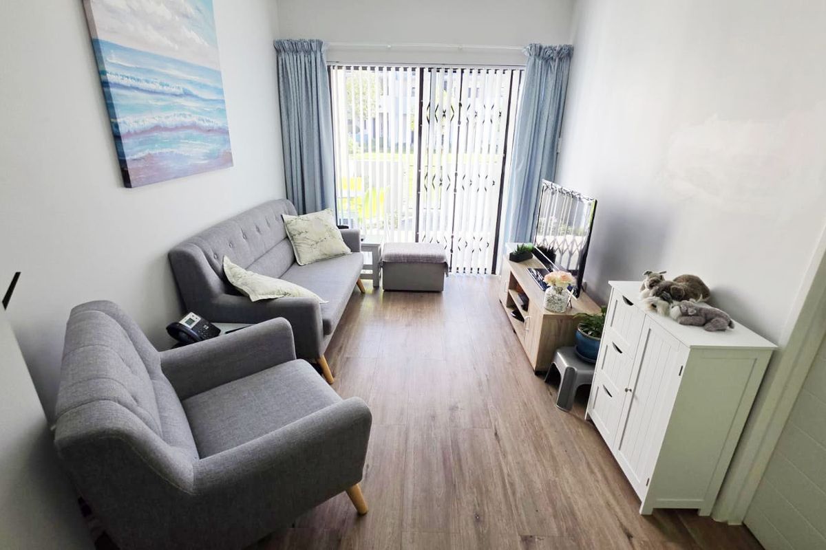 A compact living room featuring laminate flooring, a sliding glass door with security gate, and vertical blinds, offering direct access to the outdoors.