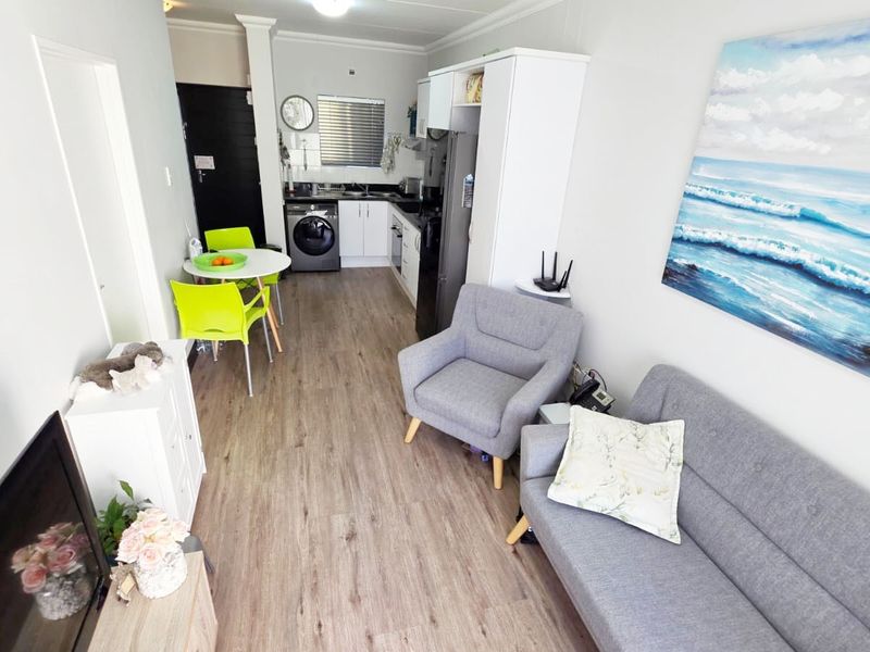 An open-plan living area featuring a compact kitchen with built-in cabinetry, integrated laundry space, and durable laminate flooring throughout.