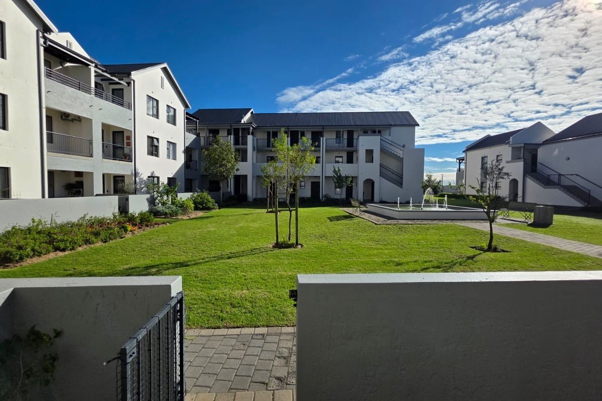 A well-maintained communal garden area within a retirement village, featuring a central water fountain, paved pathways, and surrounding multi-story residential apartment blocks.