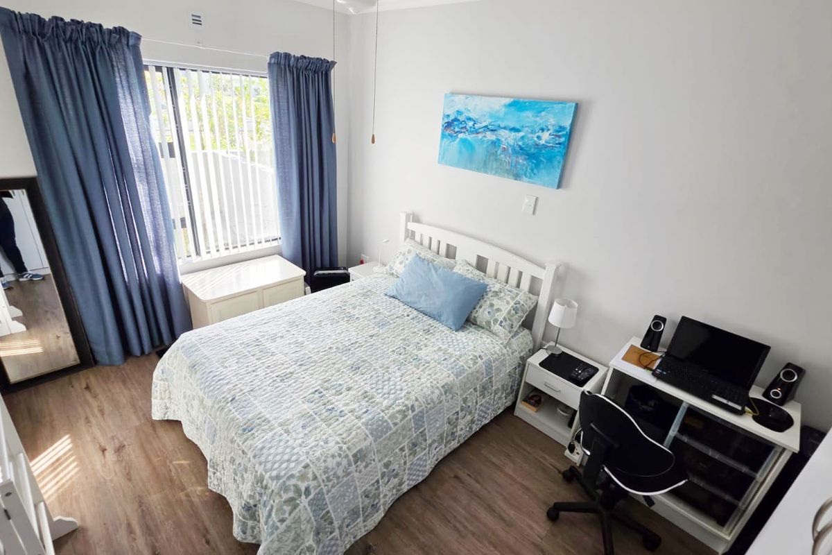 A well-maintained bedroom featuring durable laminate flooring, a ceiling fan, and large windows with vertical blinds for natural light control.