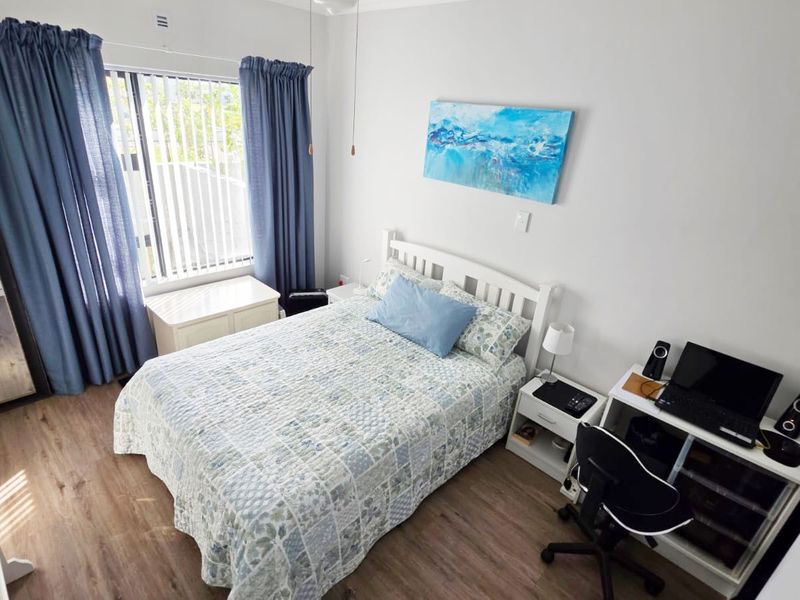 A well-maintained bedroom featuring durable laminate flooring, a ceiling fan, and large windows with vertical blinds for natural light control.