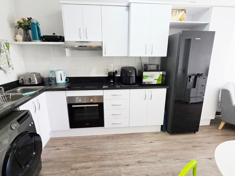 Modern kitchen featuring white cabinetry, black stone benchtops, integrated appliances, and durable timber-look flooring in a clean, functional layout.