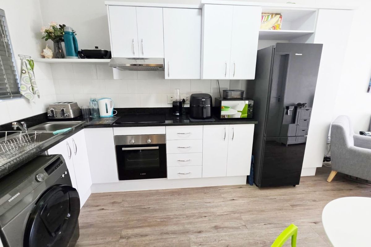 Modern kitchen featuring white cabinetry, black stone benchtops, integrated appliances, and durable timber-look flooring in a clean, functional layout.