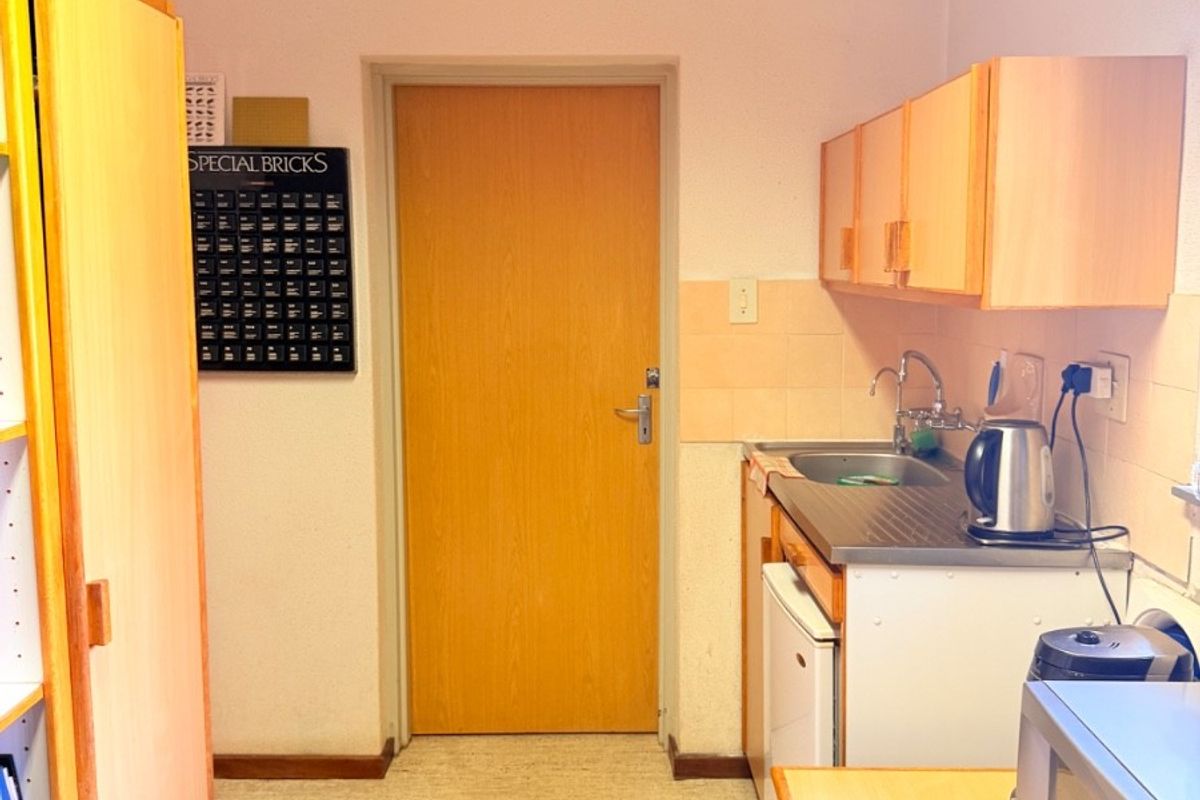 A compact kitchenette featuring basic cabinetry, a stainless steel sink, and tiled splashbacks, providing functional utility space.