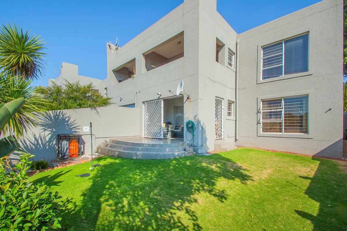 Rear view of a two-story townhouse featuring a private garden, paved patio area, and security gates on ground floor access points.