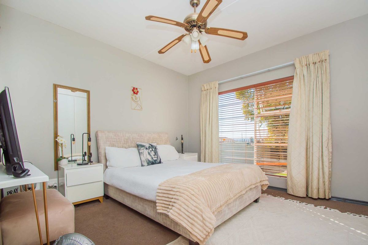 A well-lit bedroom featuring a ceiling fan, large window with blinds, and neutral wall finishes.