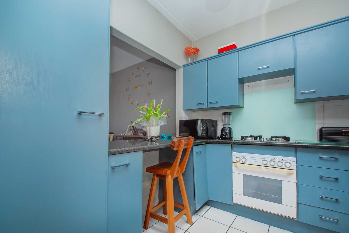 Compact kitchen featuring blue cabinetry, granite countertops, built-in oven, gas hob, and a breakfast bar pass-through to the adjacent living area.