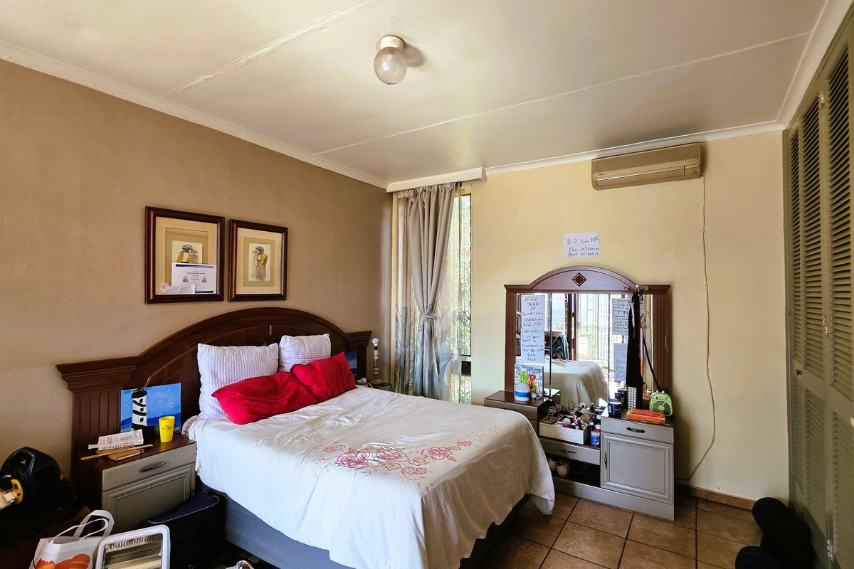 A functional bedroom featuring tiled flooring, a wall-mounted air conditioning unit, and built-in closet doors.