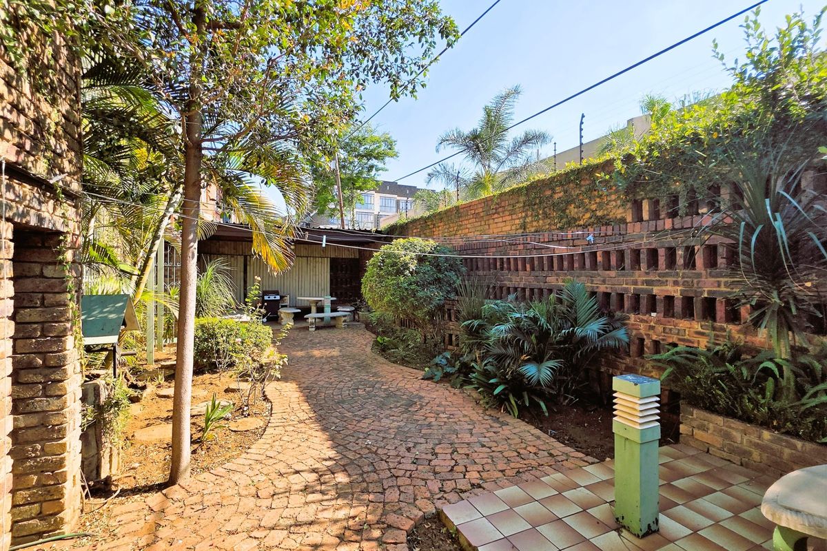 A private rear garden featuring a brick-paved pathway, established landscaping, and a decorative brick boundary wall with integrated garden lighting.