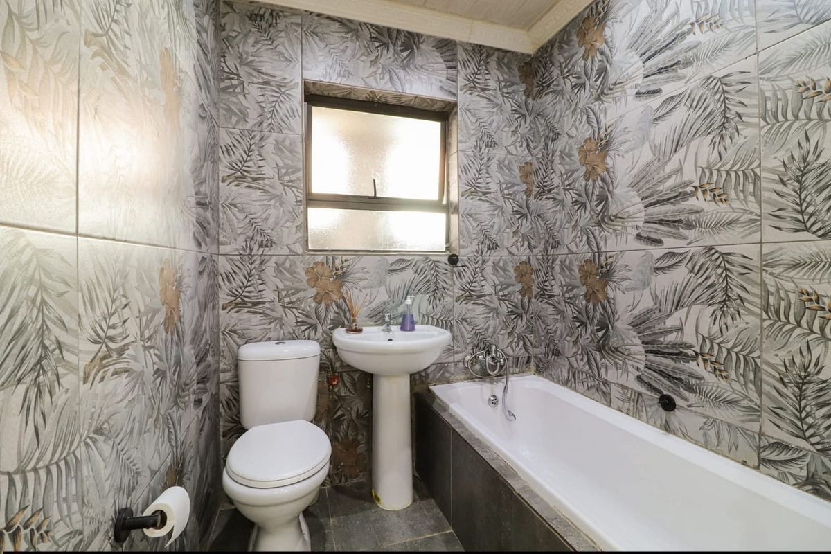 A compact bathroom featuring full-height patterned wall tiling, a pedestal basin, a standard toilet, and a built-in bathtub with a window for natural light.