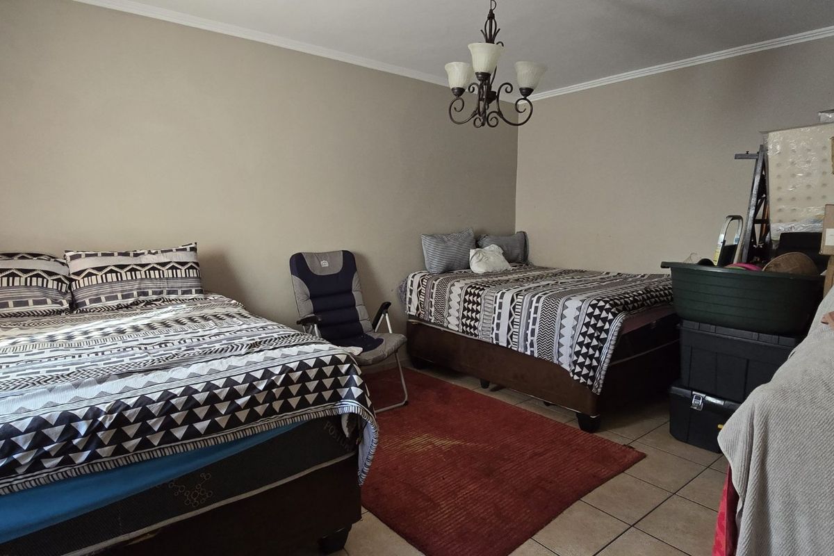 A spacious bedroom featuring tiled flooring, a central chandelier, and neutral wall tones, offering a functional layout for multiple beds.