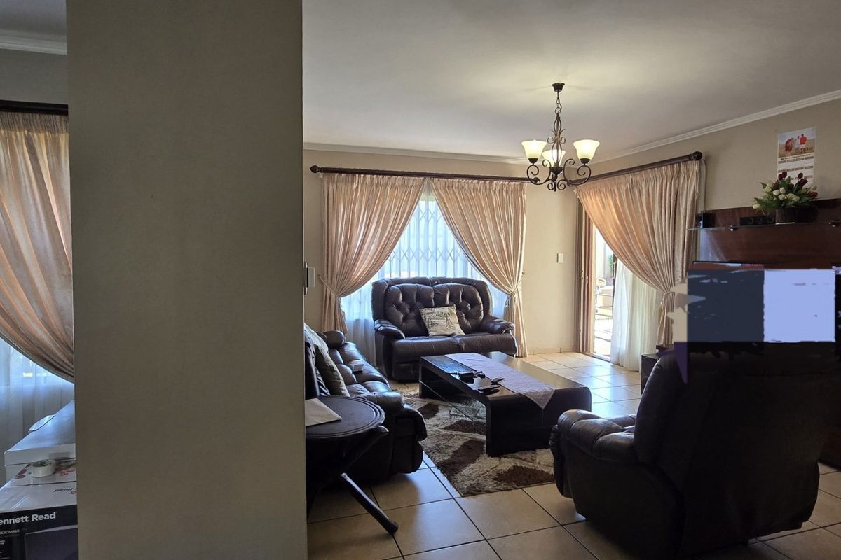 Spacious living area featuring tiled flooring, large windows with security bars, and a central chandelier, providing a comfortable and functional family space.