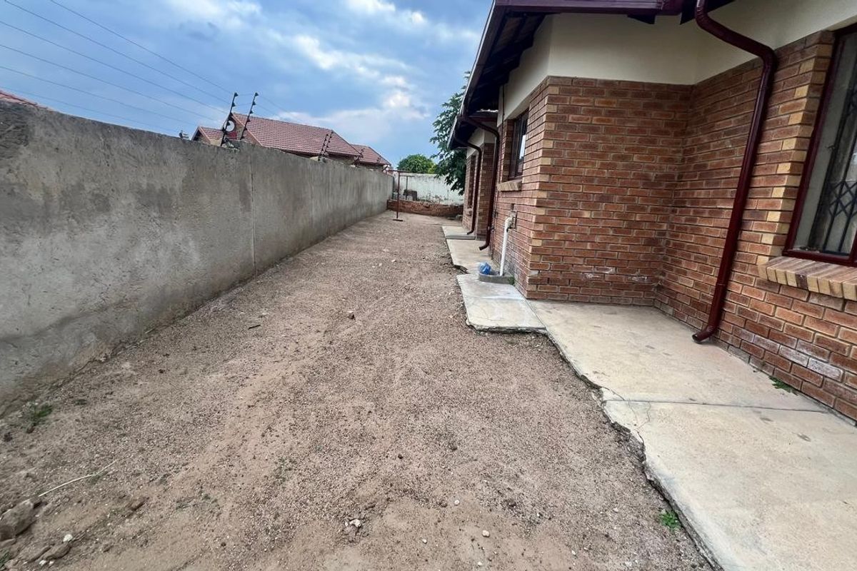 A side exterior view of the property featuring a brick facade, a concrete walkway, and an unlandscaped yard enclosed by a perimeter wall.