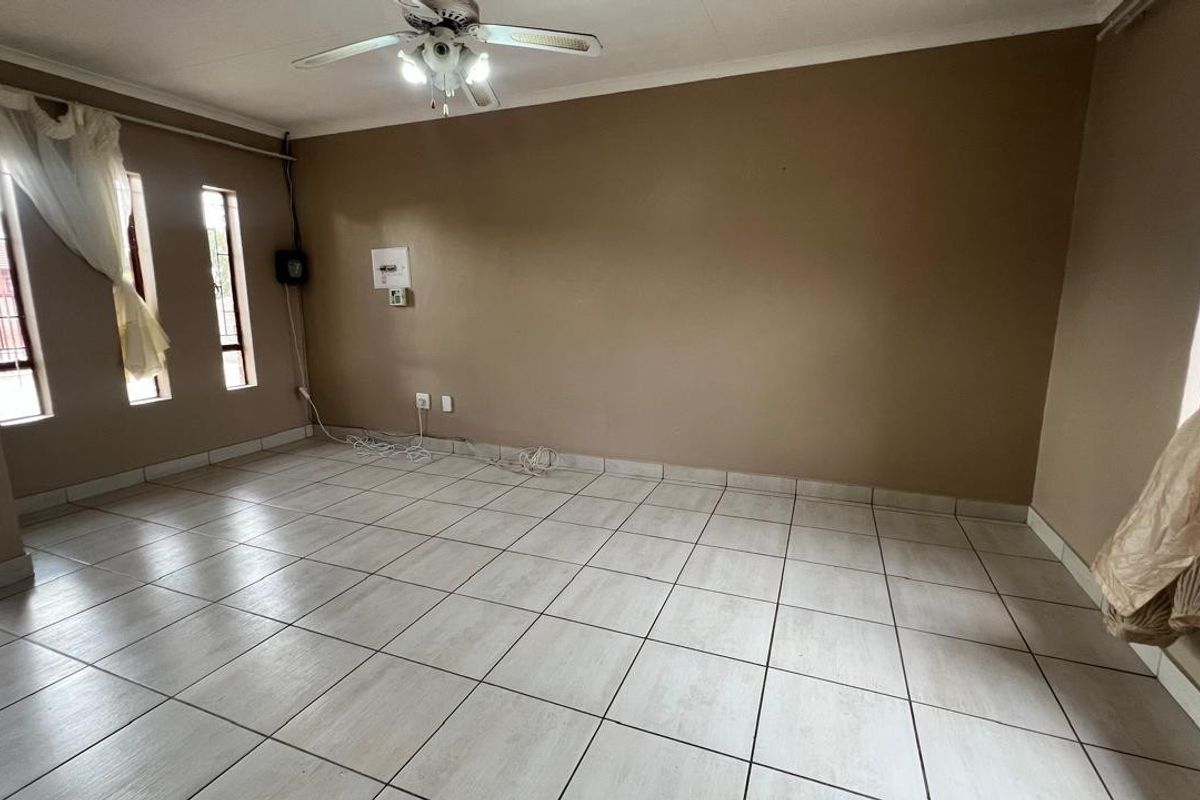A spacious, empty living room featuring neutral tiled flooring, a ceiling fan, and security bars on the windows.