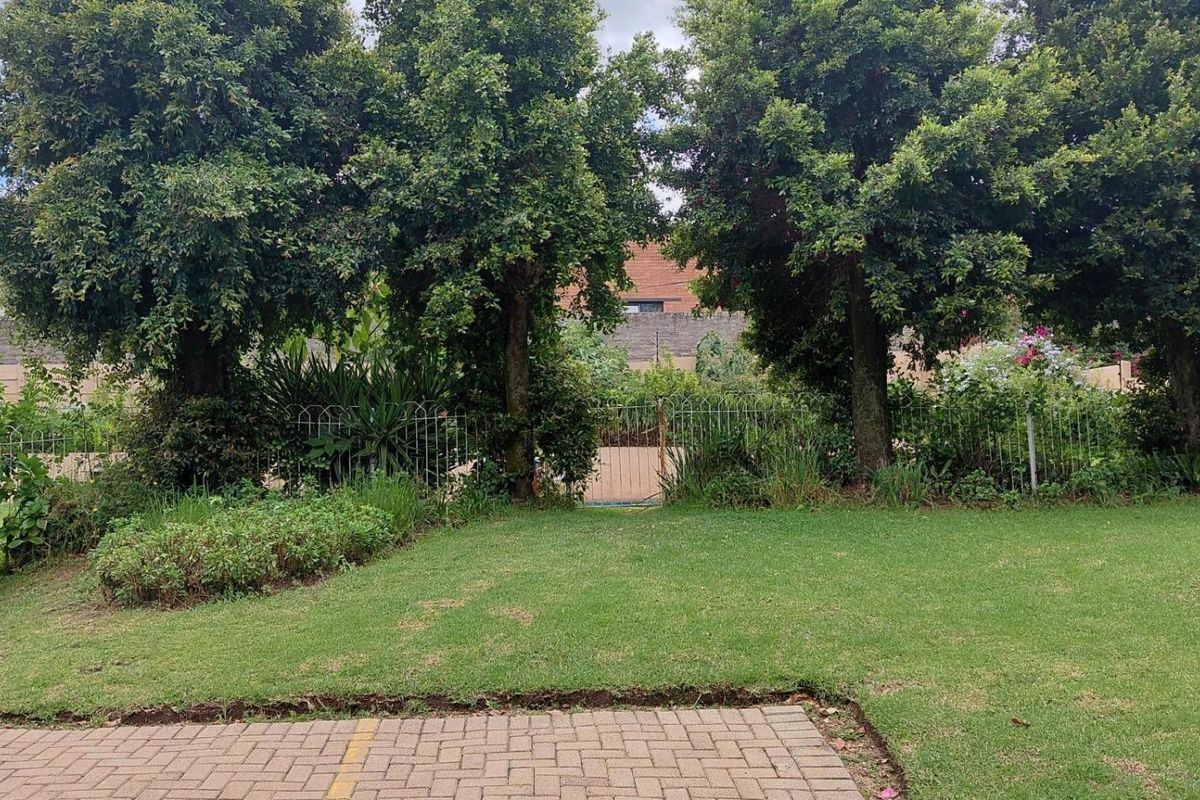 A private rear garden featuring a well-maintained lawn, mature trees, and a paved patio area enclosed by a perimeter fence.