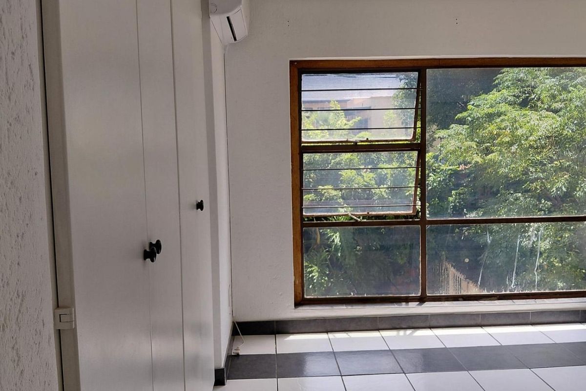 A bedroom featuring built-in cupboards, tiled flooring, and a large window providing natural light and garden views.