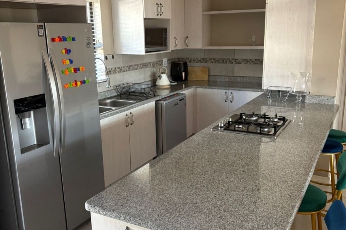 Modern kitchen featuring light wood cabinetry, granite countertops, a breakfast bar with integrated gas hob, and stainless steel sink.