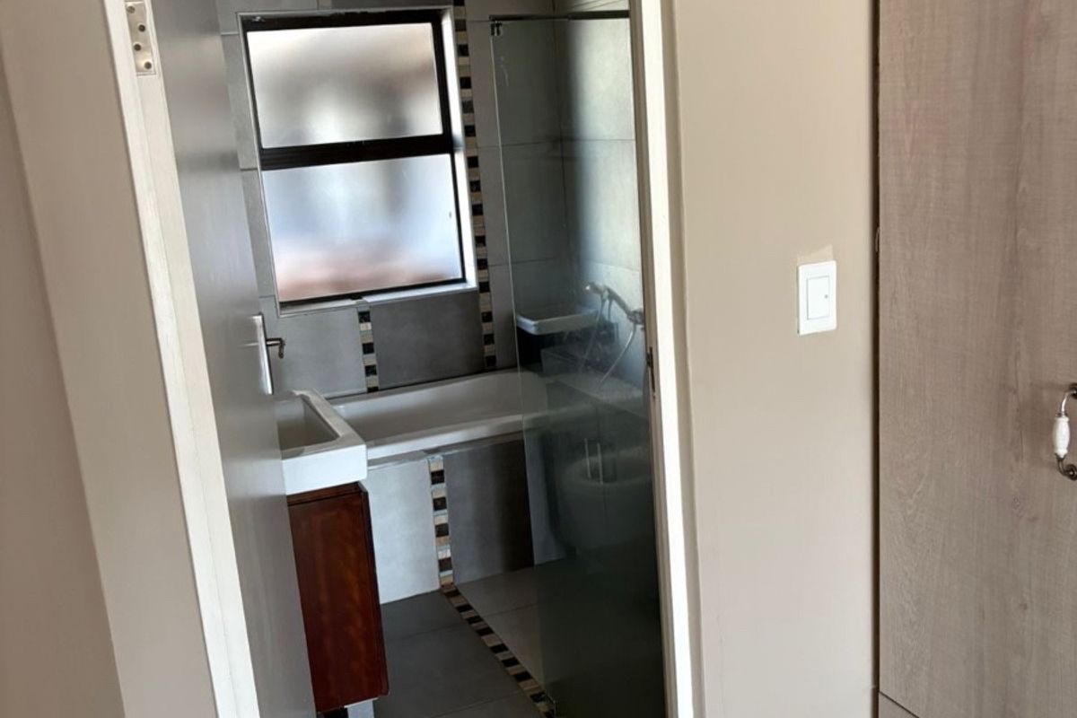 A view through a doorway into a bathroom featuring tiled flooring, a bathtub, and a glass shower enclosure, adjacent to built-in bedroom cabinetry.