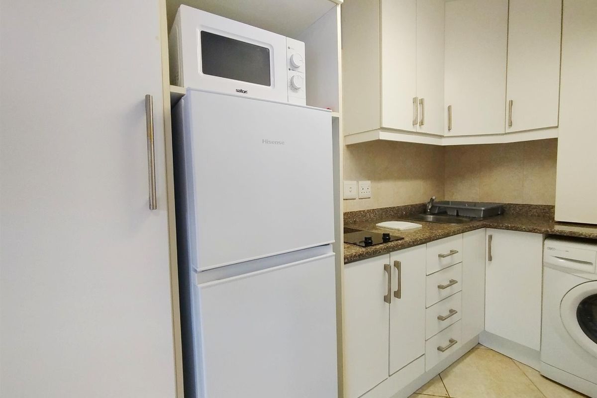 Compact kitchen featuring white cabinetry, granite countertops, an electric hob, and integrated space for a microwave and laundry appliance.