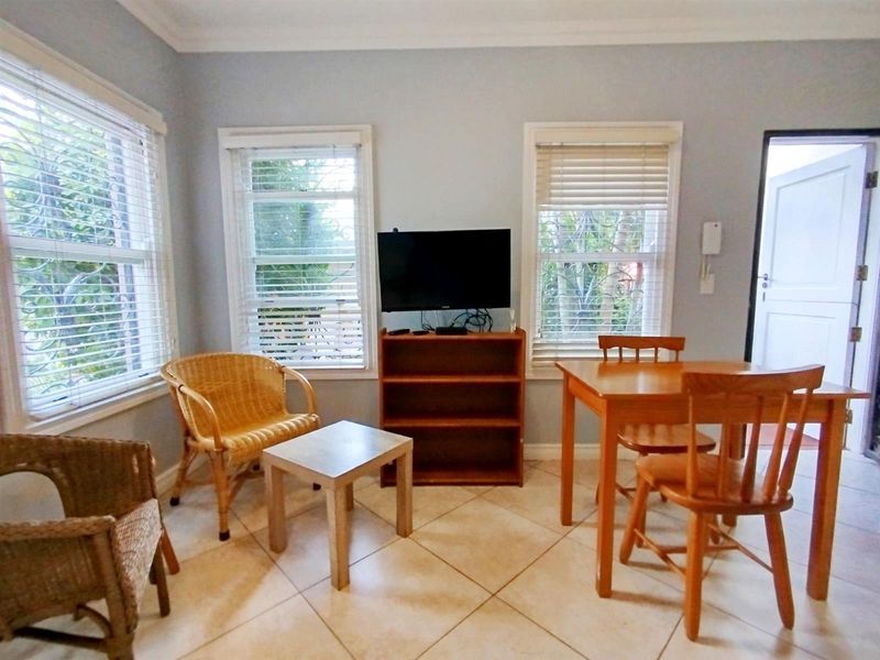 A bright living area featuring tiled flooring, large windows with venetian blinds, and decorative cornicing, providing a functional and well-lit space.
