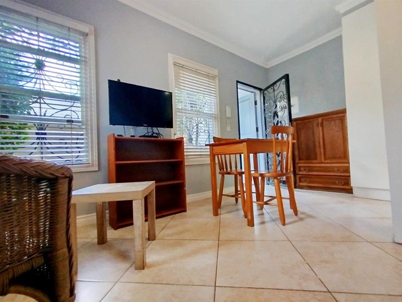 A living area featuring tiled flooring, built-in wooden cabinetry, and security gate access, providing a functional and well-lit space.