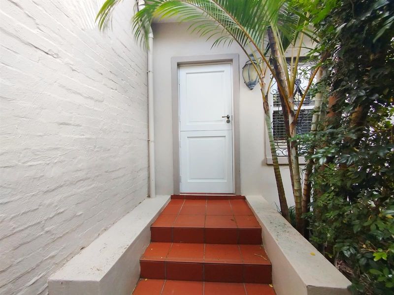 A private entrance featuring terracotta tiled steps leading to a secure door, flanked by painted brick walls and established greenery.