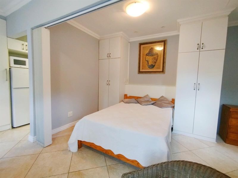 A bedroom featuring built-in cupboards, tiled flooring, and coving, with an adjacent view into a kitchen area.