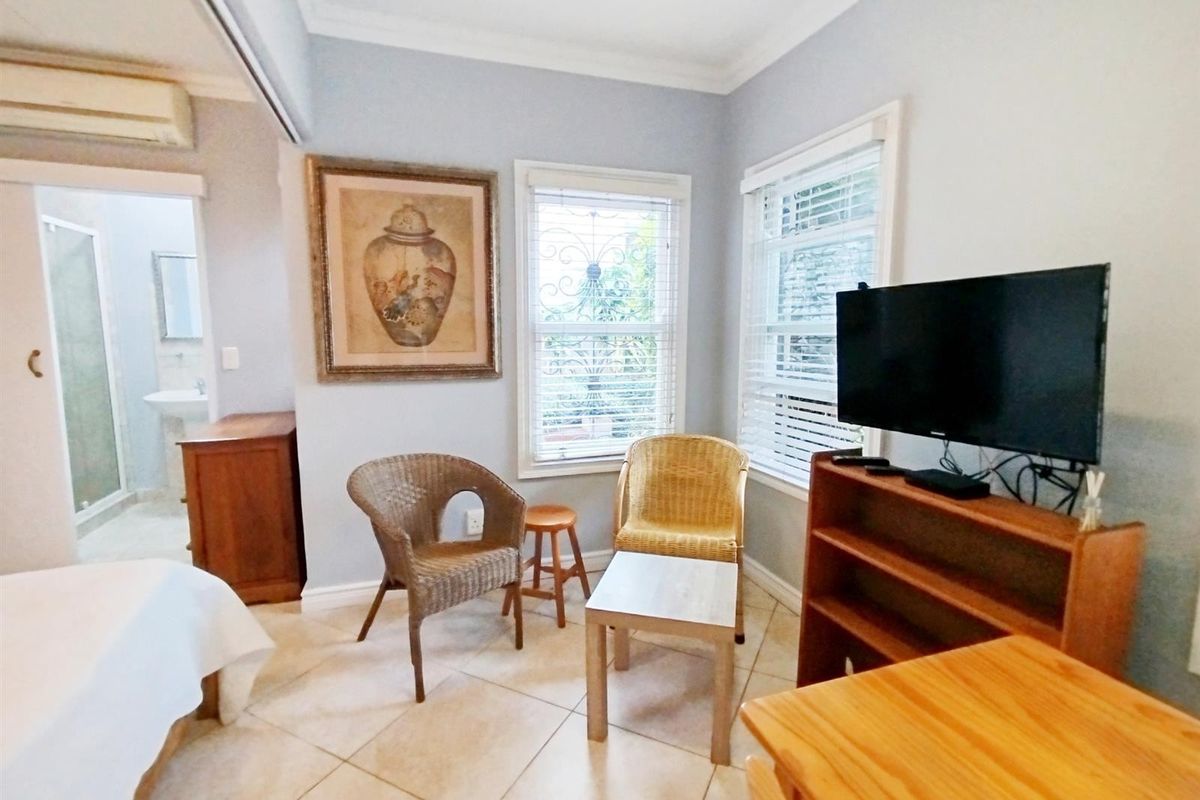 A bedroom featuring tiled flooring, split-system air conditioning, and an en-suite bathroom, with windows fitted with security bars and venetian blinds.