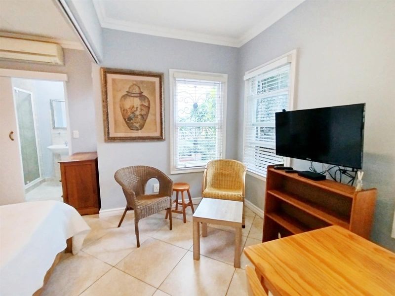A bedroom featuring tiled flooring, split-system air conditioning, and an en-suite bathroom, with windows fitted with security bars and venetian blinds.