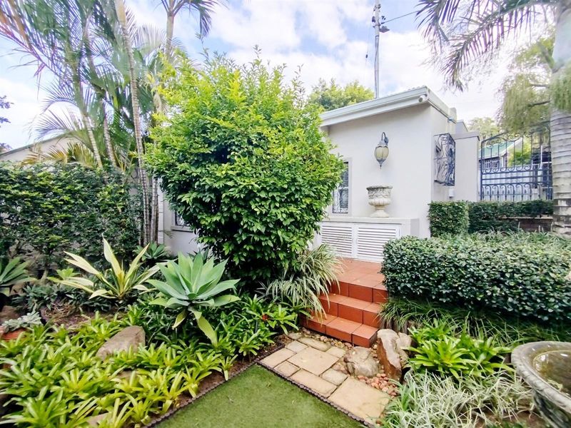 A well-maintained garden area featuring landscaped greenery, stone paving, tiled steps leading to a building entrance, and secure wrought iron gate access.