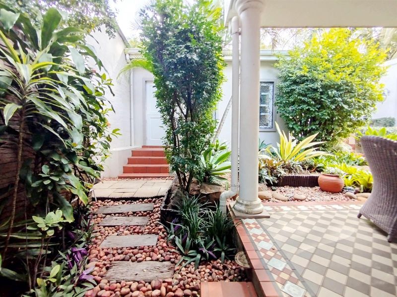 A charming rear courtyard featuring a tiled patio area, stone pathway, and established garden beds leading to an exterior entrance.