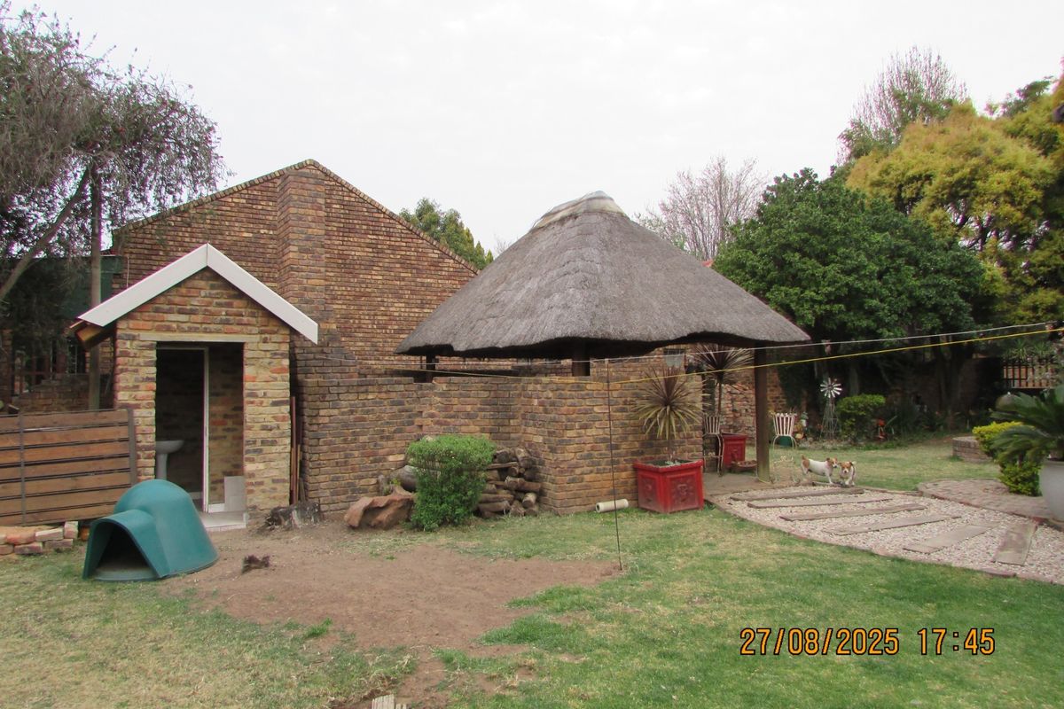 Rear garden area featuring a facebrick townhouse exterior and a traditional thatch lapa entertainment structure.